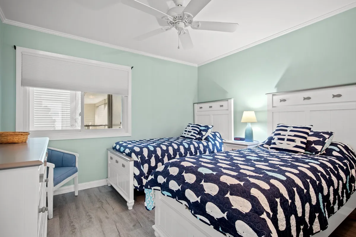 A bright and inviting bedroom with twin beds dressed in whale-patterned bedding, white furniture, and a window flooding the room with natural light. The arrangement is ideal for children or friends sharing a space.