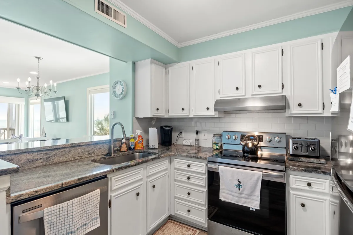 A modern kitchen gleams with granite countertops, stainless steel appliances, white cabinetry, and light blue walls. The spacious layout is perfect for cooking, entertaining, and participating in family food traditions.