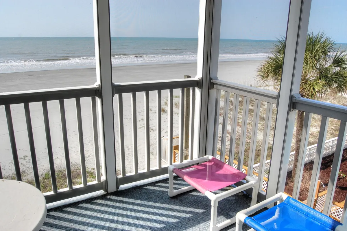A tranquil view from an outdoor seating area looking out onto the beach, palm trees, and sea. The setup invites group members to gather for relaxed conversations, enjoy the scenery together, or unwind with a book in hand.