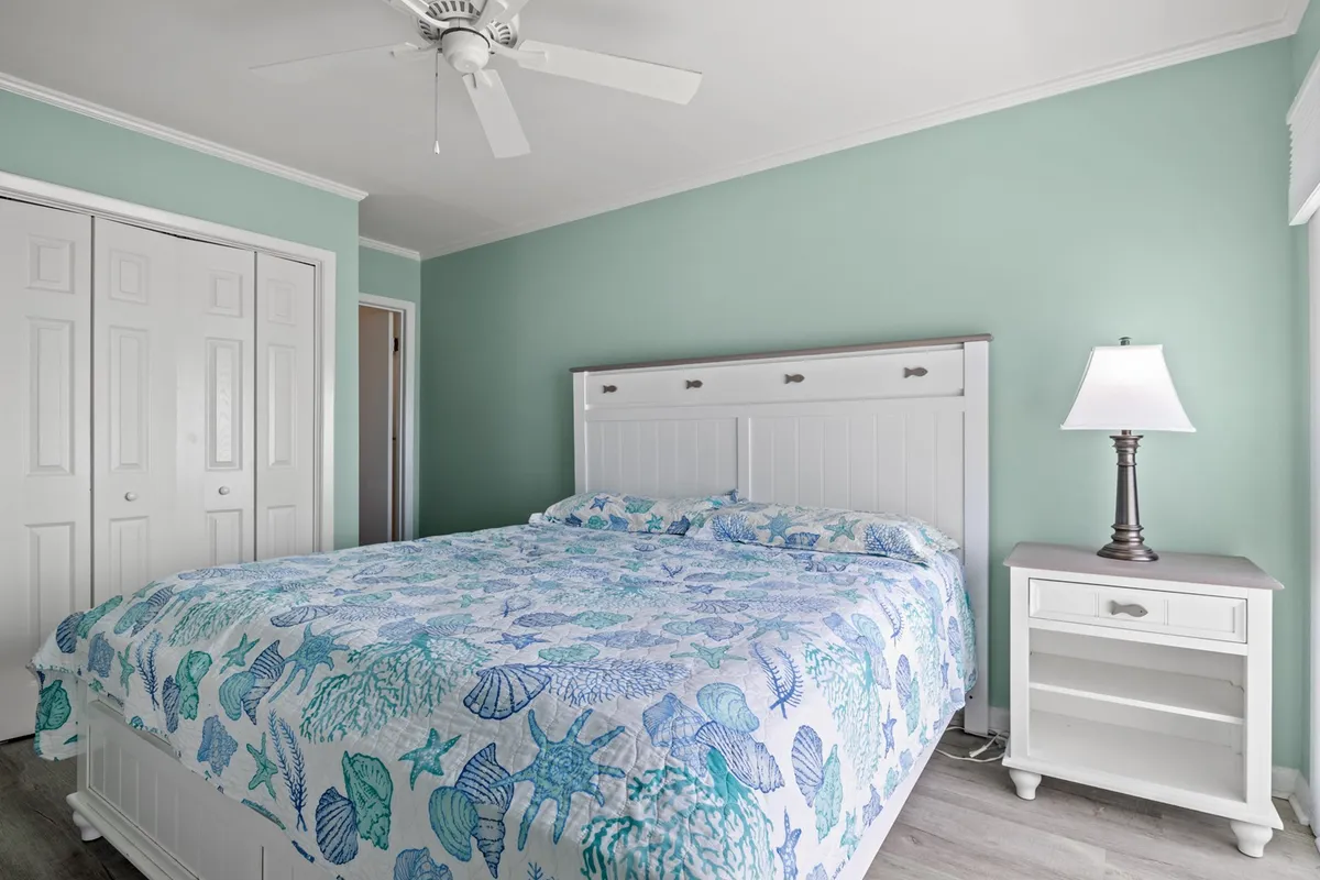 A bedroom with a patterned bedspread, nightstand and lamp, and soothing wall colors. The overall feel is serene and tailored for relaxation, suggesting a welcoming place to recharge.