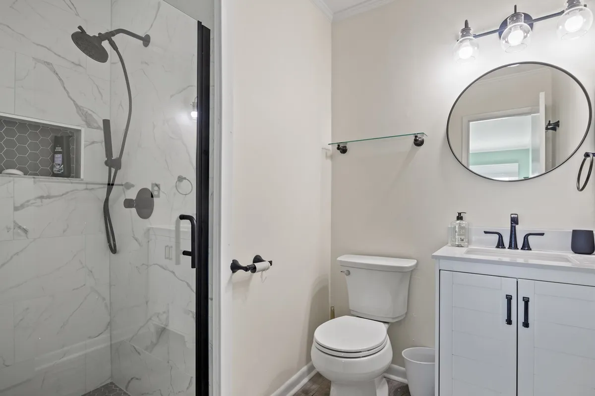 A renovated bathroom featuring a glass-enclosed shower, vanity with sink, round mirror, and stylish lighting fixtures. The contemporary design and inviting mood promise a spa-like experience for guests.