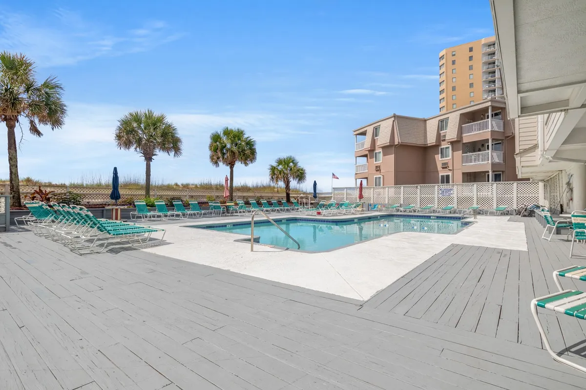A sun-drenched resort pool surrounded by palm trees and lounge chairs, embodying a leisurely, resort-style atmosphere. The pool glistens under the sun, inviting residents for a refreshing swim or lazy afternoon lounging.