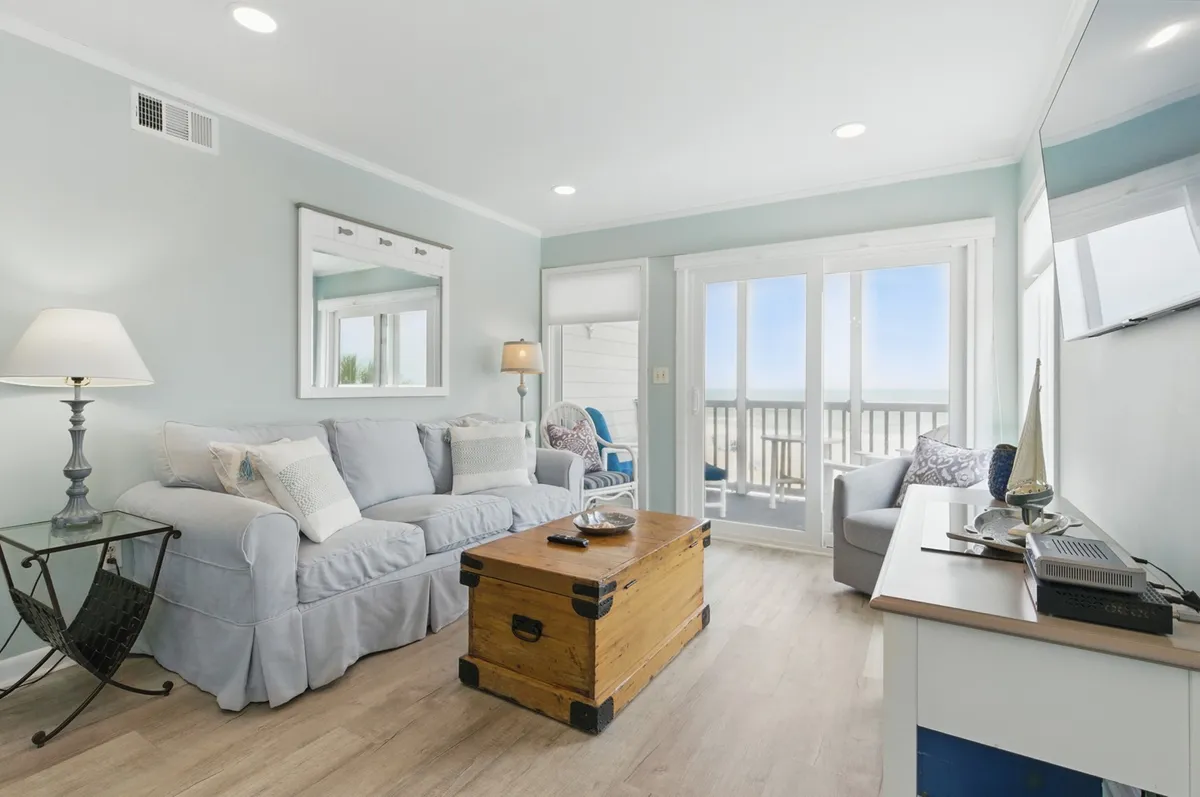 A cozy living area with a sofa, coffee table, large windows offering natural light, a lamp, and a television. The atmosphere is comfortable and homey, suggesting a space ideal for relaxing after handling daily tasks like laundry.