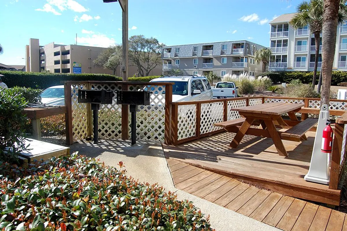 A spacious grilling area with a wooden picnic table, grilling station, and lush green landscaping. The casual setting encourages social gatherings, sunset picnics, or festive cookouts with friends and family.