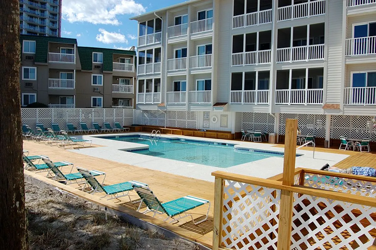 This image features a sparkling swimming pool surrounded by lounge chairs and the resort's buildings. The area is enclosed by a fence and invites guests to relax poolside, socialize, or enjoy a dip after a day at the beach.